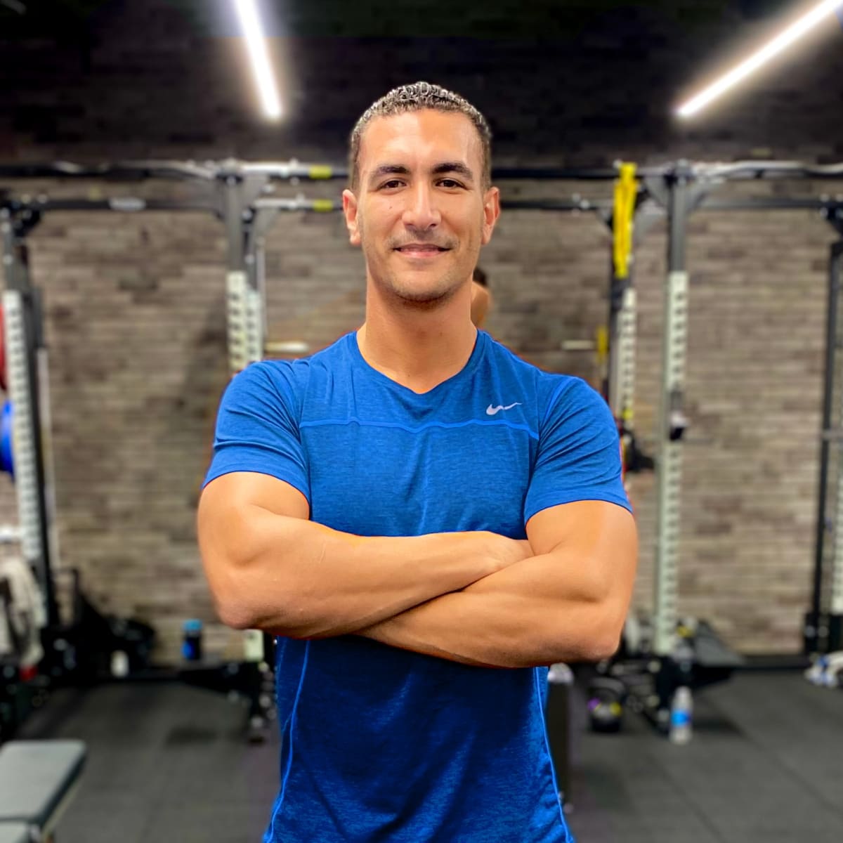 Coach fathi, an Arabic speaking online personal trainer, smiling with folded arms inside a modern gym setting