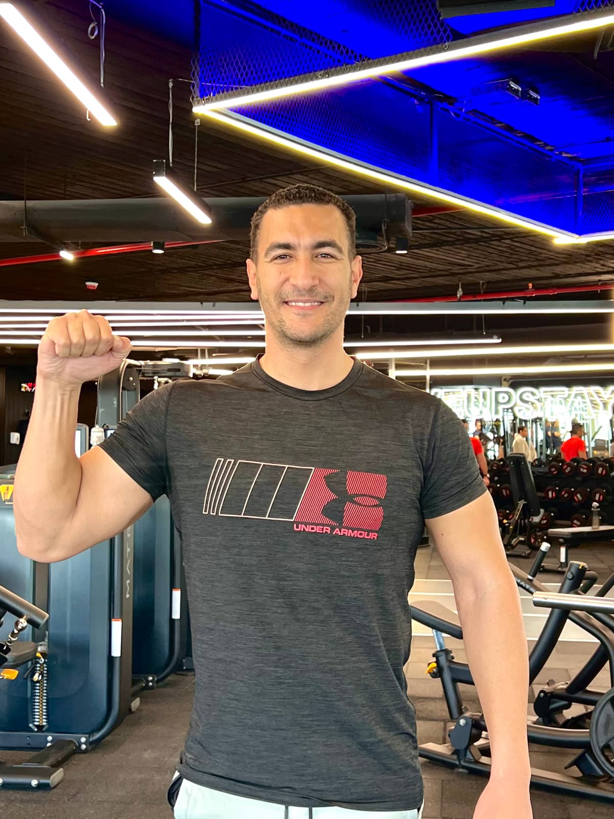 Coach fathi, an Arabic speaking online personal trainer, smiling and gesturing a fist pump of success in a gym