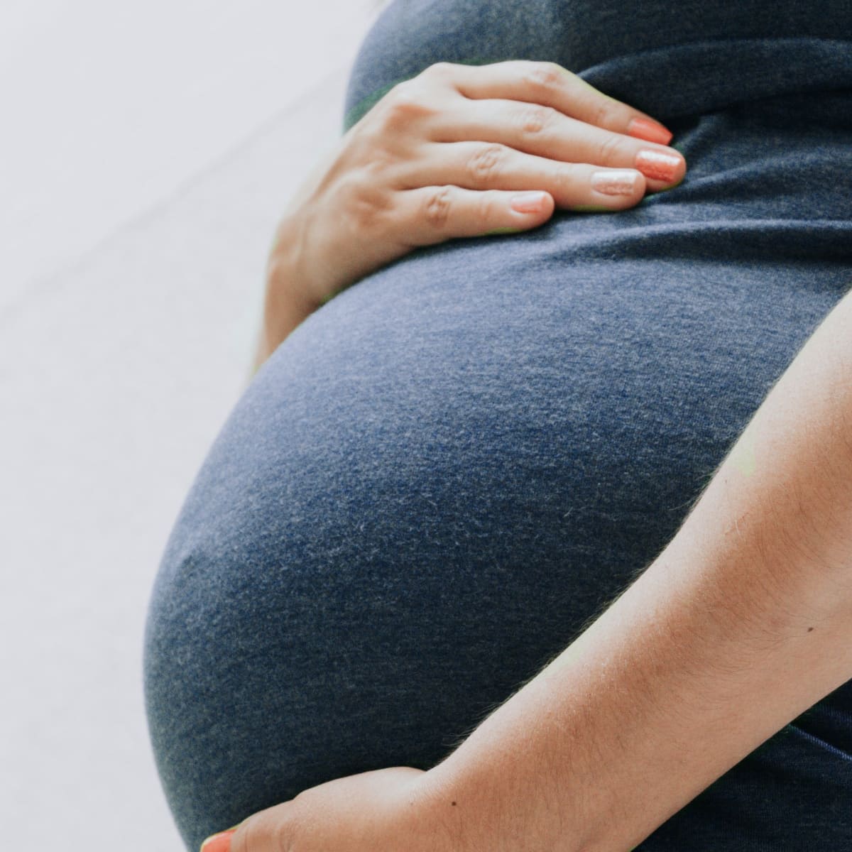 A close-up shot of a pregnant woman cradling her belly in a comfortable grey shirt, emphasizing how to Stay Active During Pregnancy